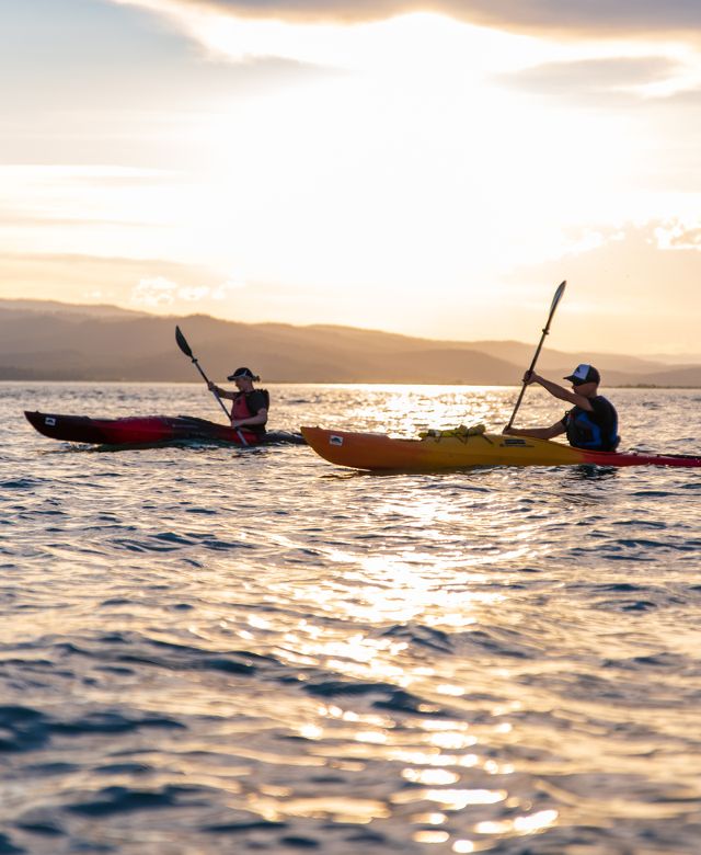 Two kayakers paddling in Flathead Lake against a setting sun